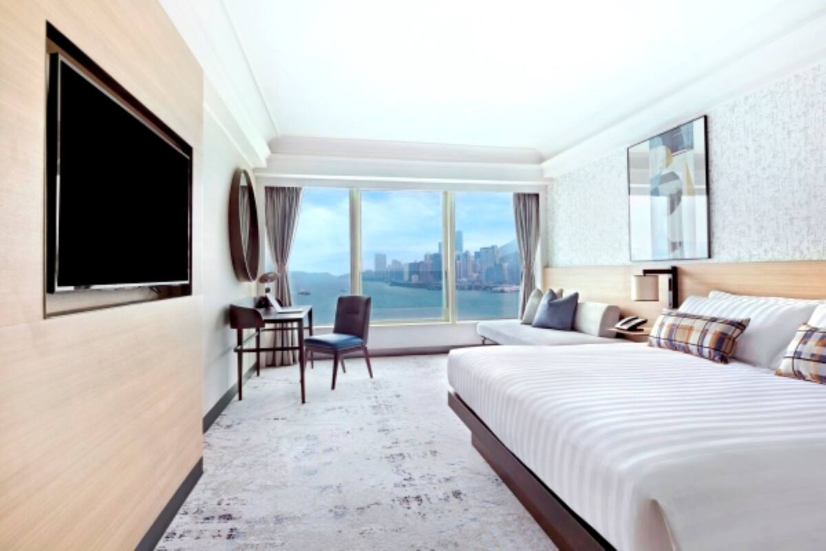 A hotel room with a large bed, a desk with a chair, a TV, and a city view.