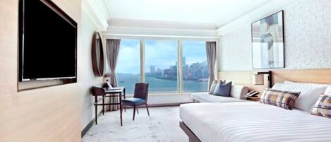 A hotel room with a large bed, a desk with a chair, a TV, and a city view.
