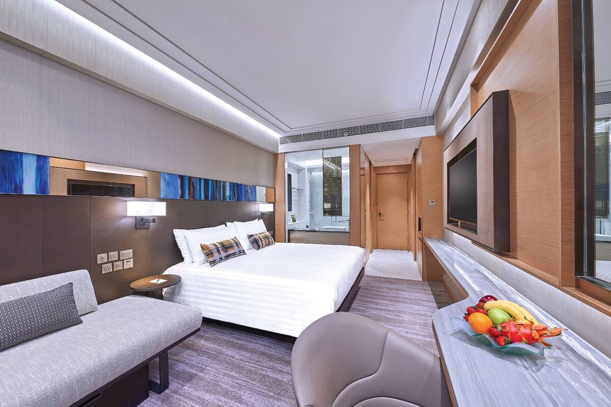 A modern hotel room with a large bed, a sofa, a TV, and a fruit bowl.