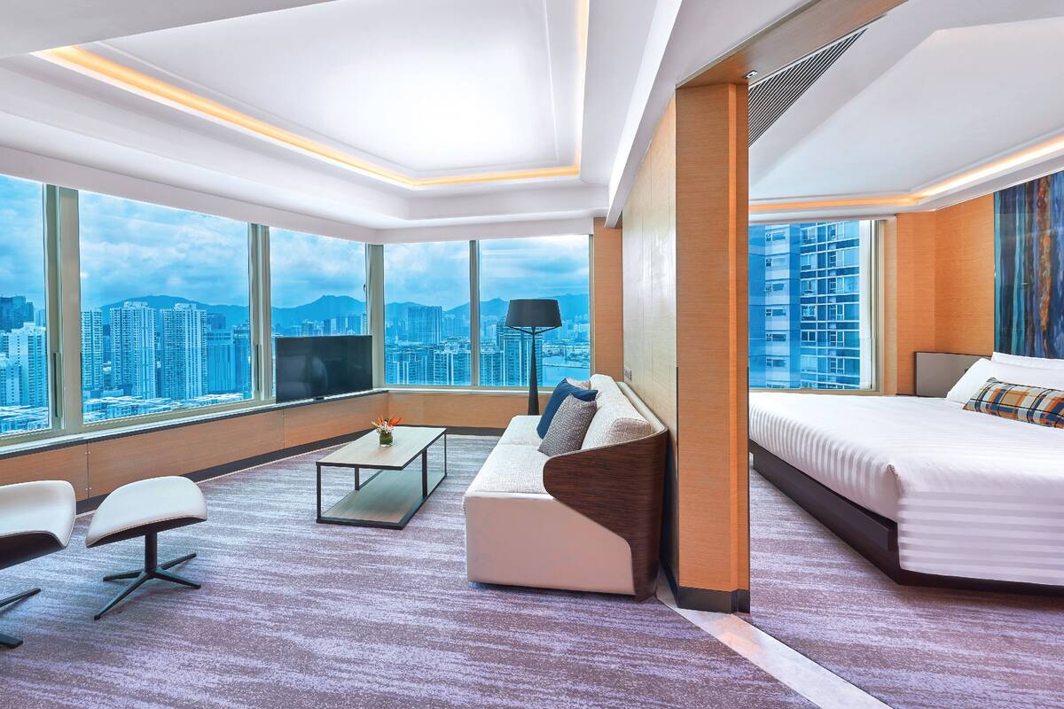 A modern hotel room with a large window, a sofa, a bed, and a coffee table.