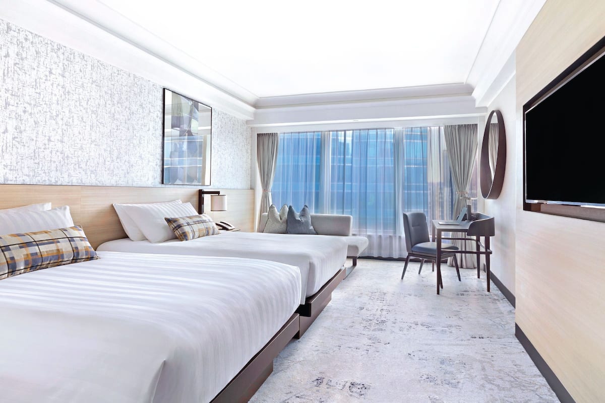 A hotel room with two beds, a desk, and a large window with curtains.