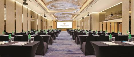 A conference room with rows of tables, chairs, and a large screen at the front.