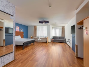 Una habitación de hotel con cama, escritorio, sofá y televisor.