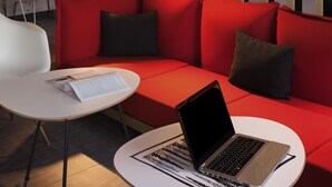 Un área de descanso moderna con un sofá rojo, una mesa blanca con una computadora portátil y una silla blanca.