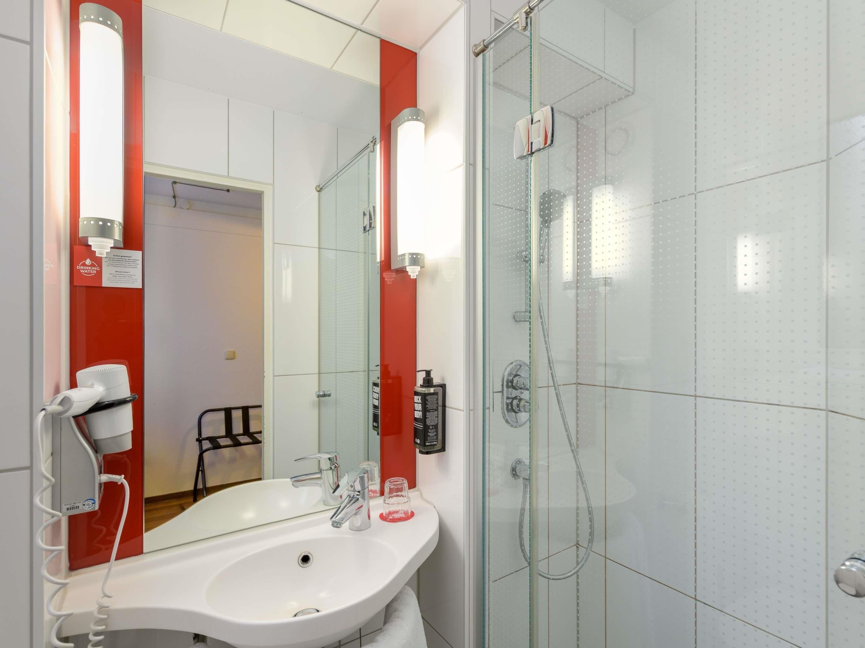 A modern bathroom with a white sink, a glass shower enclosure, and a red accent wall.