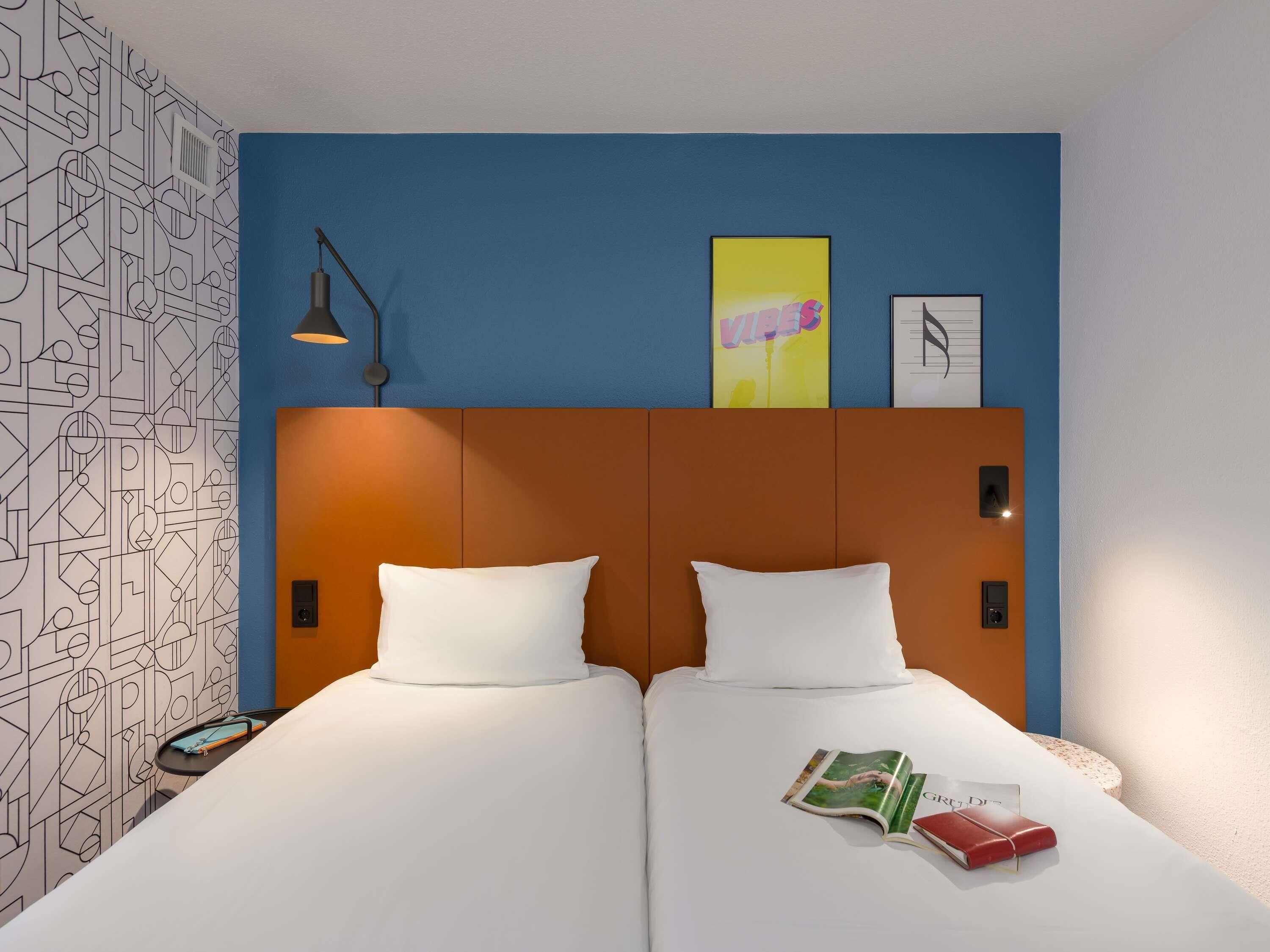 A hotel room with a modern design, featuring a large bed with white linens, a headboard with a geometric pattern, and a wall with a geometric wallpaper.