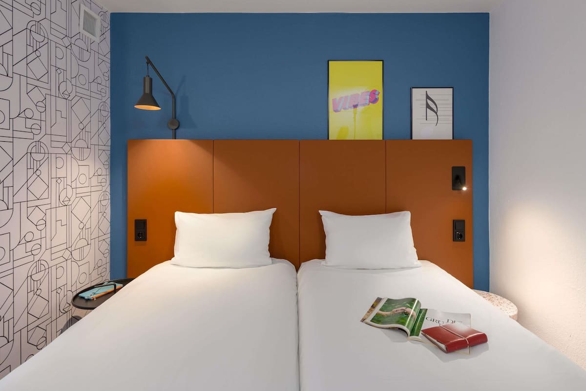 Habitación de hotel con diseño moderno, que incluye una cama grande con ropa blanca, cabecera con patrón geométrico y pared con papel tapiz geométrico.