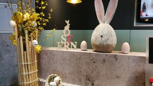 Un mostrador de recepción con una decoración de Pascua que incluye una figura de conejo, un jarrón con flores amarillas y un nido con huevos.