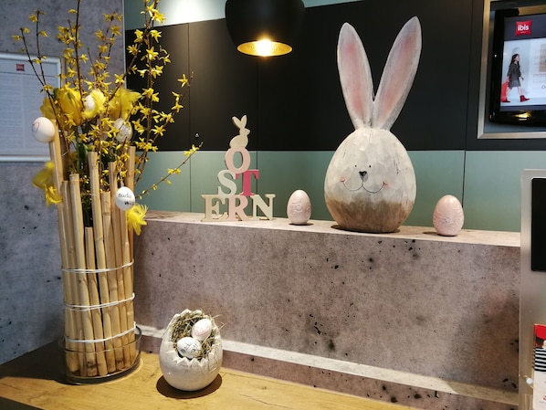 Un mostrador de recepción con una decoración de Pascua que incluye una figura de conejo, un jarrón con flores amarillas y un nido con huevos.