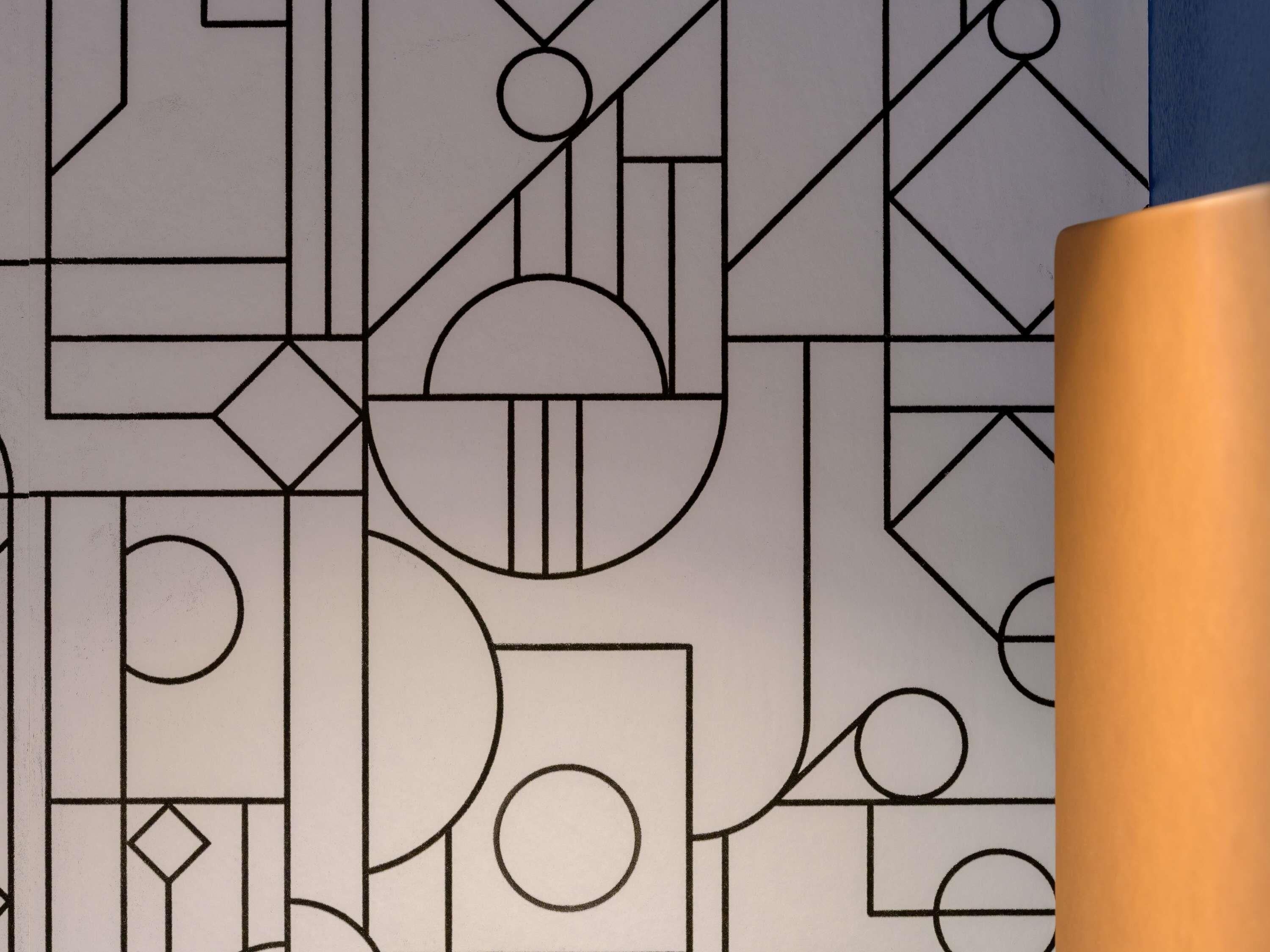 A geometric pattern on a wall with a cylindrical object in the foreground.