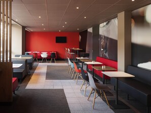 Een modern restaurantinterieur met zitjes, tafels en een rode accentmuur.