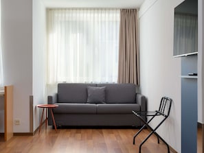 A modern living room with a sofa, a small table, a chair, and a television on a stand. - ibis Nürnberg Hauptbahnhof (Nuremberg)