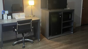 A hotel room with a desk, chair, television, and a mirror.