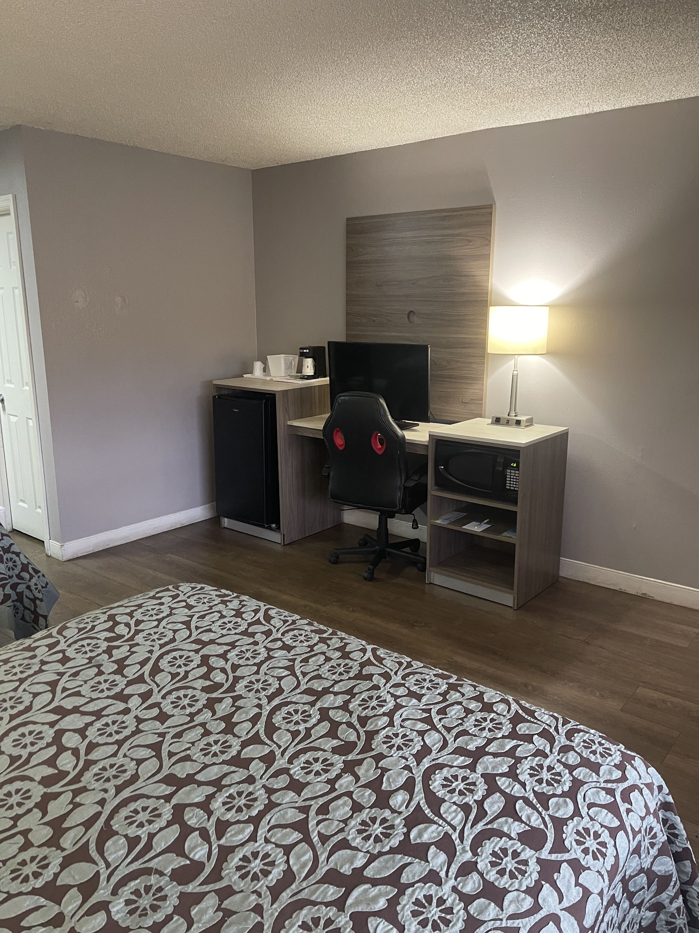 Ein Hotelzimmer mit einem Bett, einem Schreibtisch mit Computer, einem Stuhl, einer Lampe und einer Mikrowelle.
