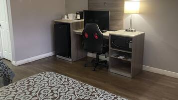 Ein Hotelzimmer mit einem Bett, einem Schreibtisch mit Computer, einem Stuhl, einer Lampe und einer Mikrowelle.