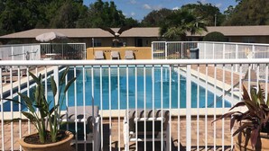 A pool area with a white fence, lounge chairs, and potted plants.