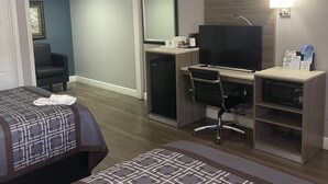A hotel room with a bed, desk, chair, TV, and a small kitchenette.