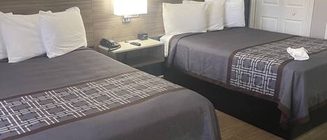 A hotel room with two beds, a nightstand with a lamp, a clock, and a door.