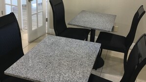 A room with two granite-topped tables and four black chairs. A flat-screen TV is mounted on the wall.