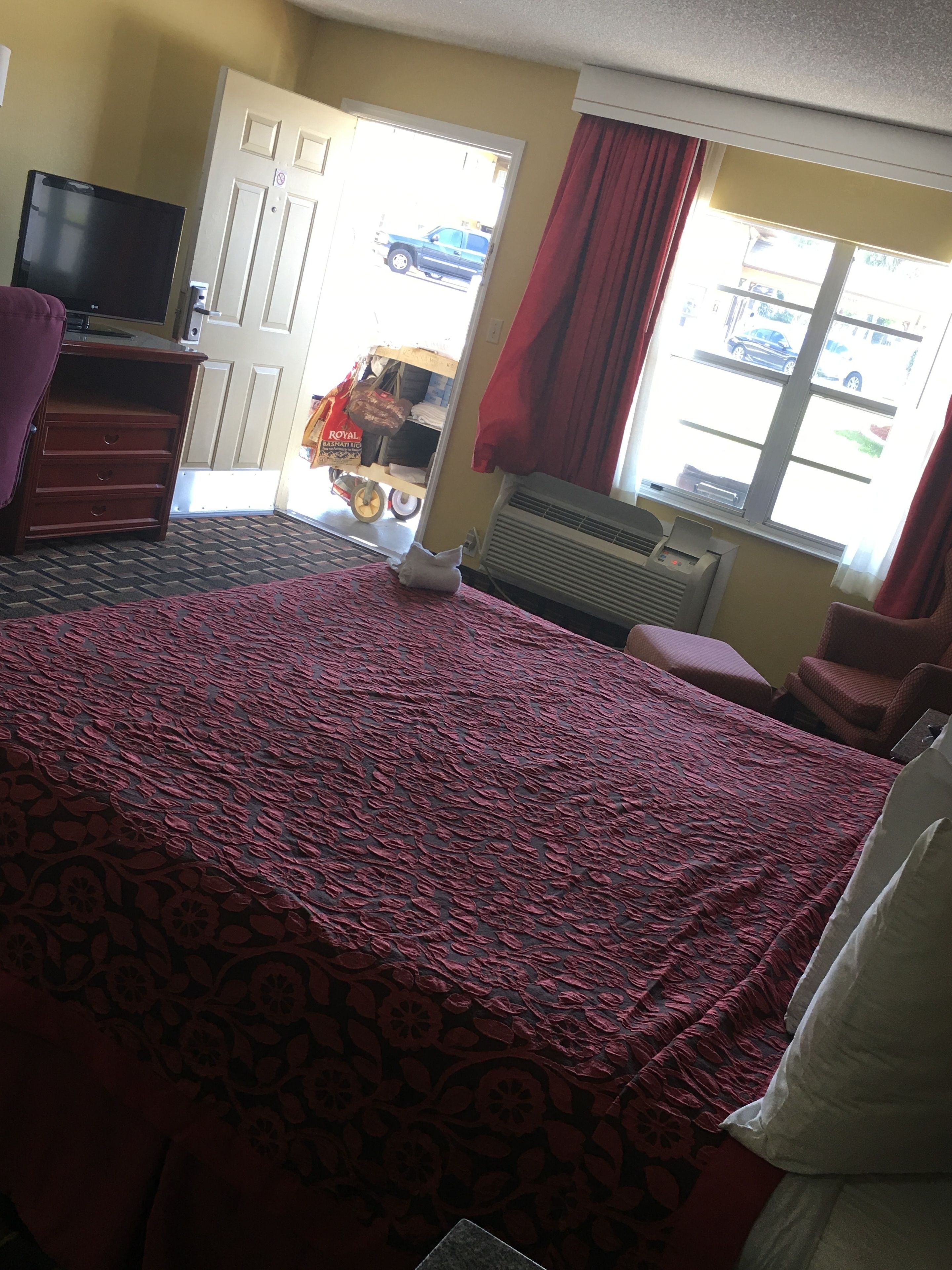 A hotel room with a bed, a TV, a dresser, and a window with a view of the street.