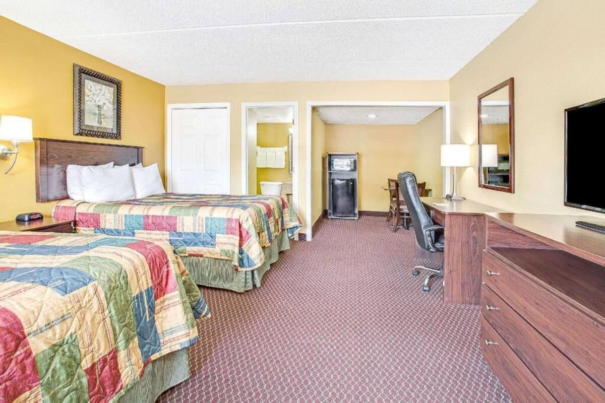 A hotel room with two beds, a desk, a chair, a television, and a refrigerator.
