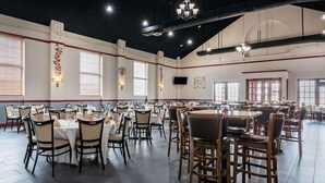 Un vaste espace dédié à la salle à manger, avec de nombreuses tables et chaises, de grandes fenêtres et des luminaires fixés au mur.