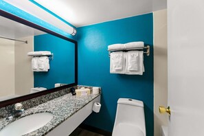 A bathroom with a blue wall, white sink, and toilet. There are towels hanging on a rack and a mirror above the sink.