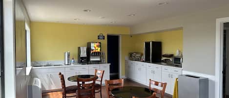 A compact kitchen with a dining area, featuring a coffee machine, refrigerator, and a small island with a sink.