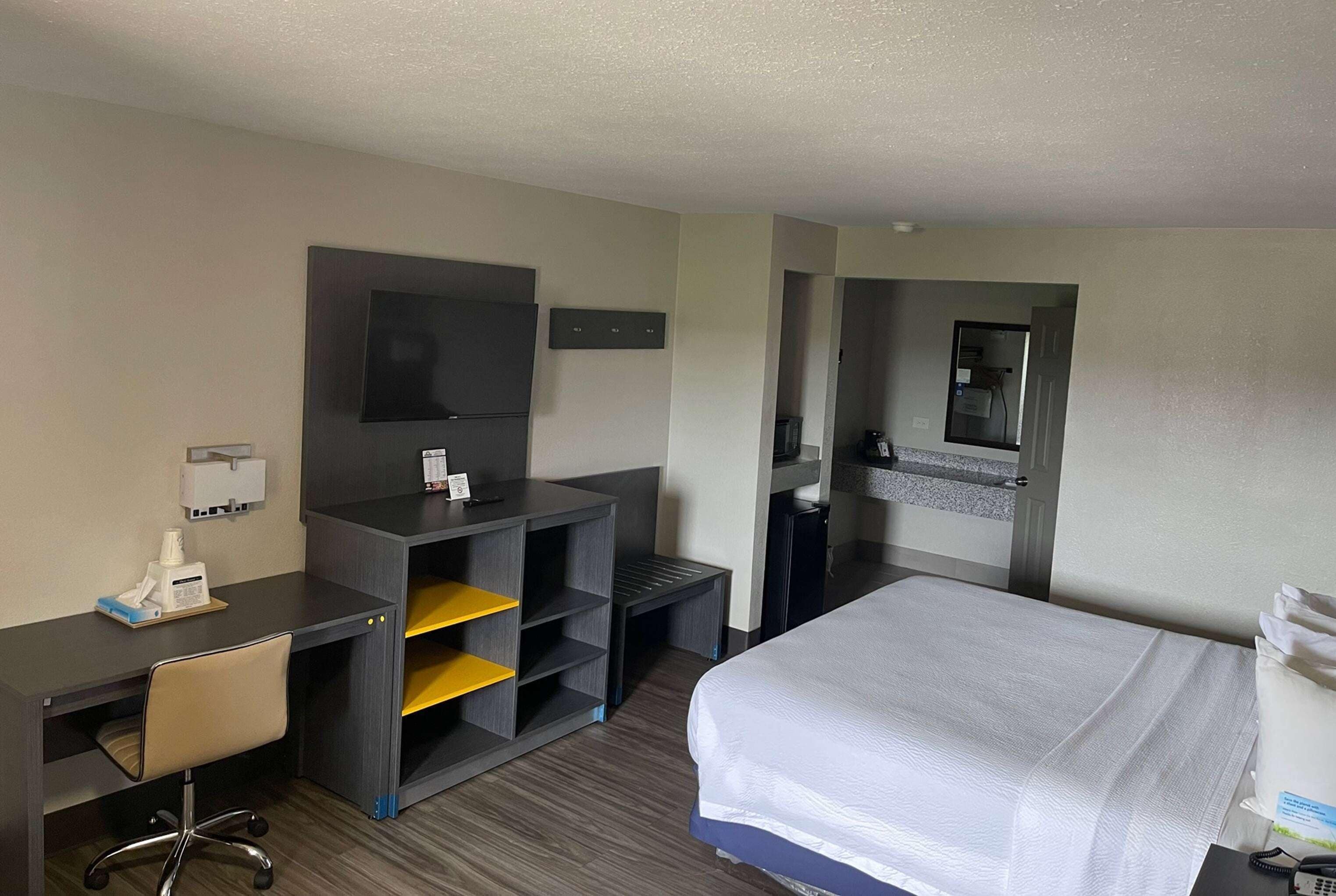 Une chambre d’hôtel équipée d’un lit, d’un bureau, d’une chaise et d’un téléviseur fixé au mur.