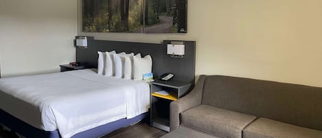 Een hotelkamer met een bed, een sofa, een klein tafeltje, een nachtkastje met een telefoon en een boslandschap op de muur.