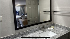Un baño con un espejo grande, encimera de granito, lavamanos y un perchero para toallas.