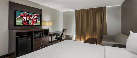 Een hotelkamer met een bed, een bureau, een televisie, een stoel en een raam met gordijnen.