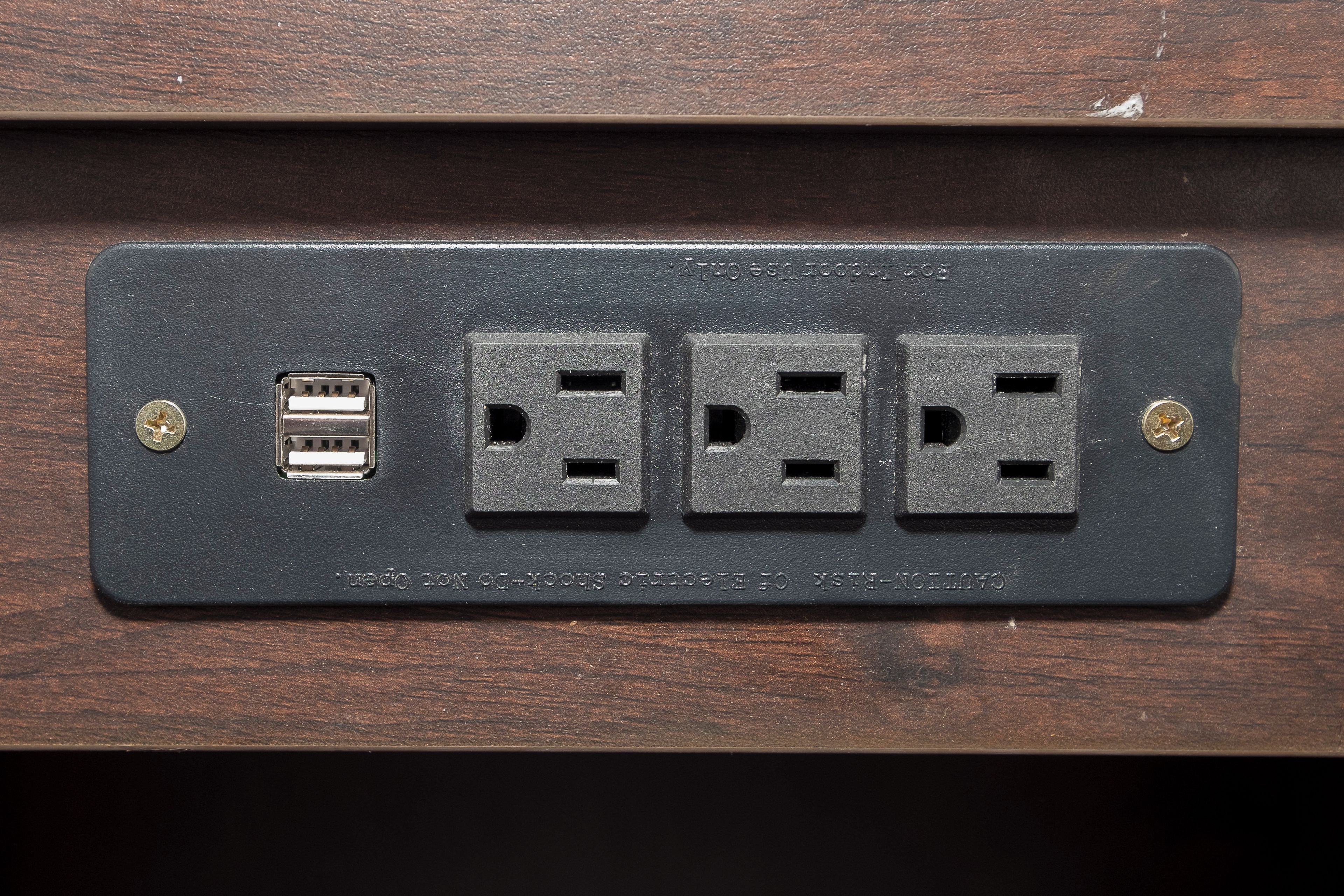 A wall-mounted electrical outlet with four sockets, including a USB port, on a wooden surface.
