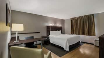Habitación de hotel con cama, mesita de noche, lámpara, silla y vistas al exterior.