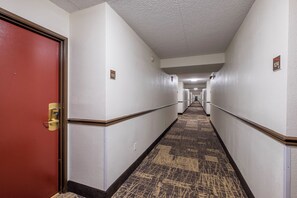 Un pasillo de hotel con una puerta roja, paredes blancas y una alfombra estampada.