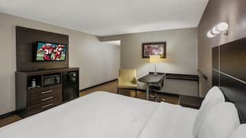 A hotel room with a bed, a television, a desk with a chair, a lamp, and a framed picture on the wall.