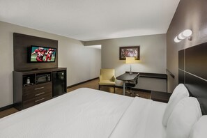 Habitación de hotel con una cama, televisión, escritorio con silla, lámpara y un cuadro en la pared.