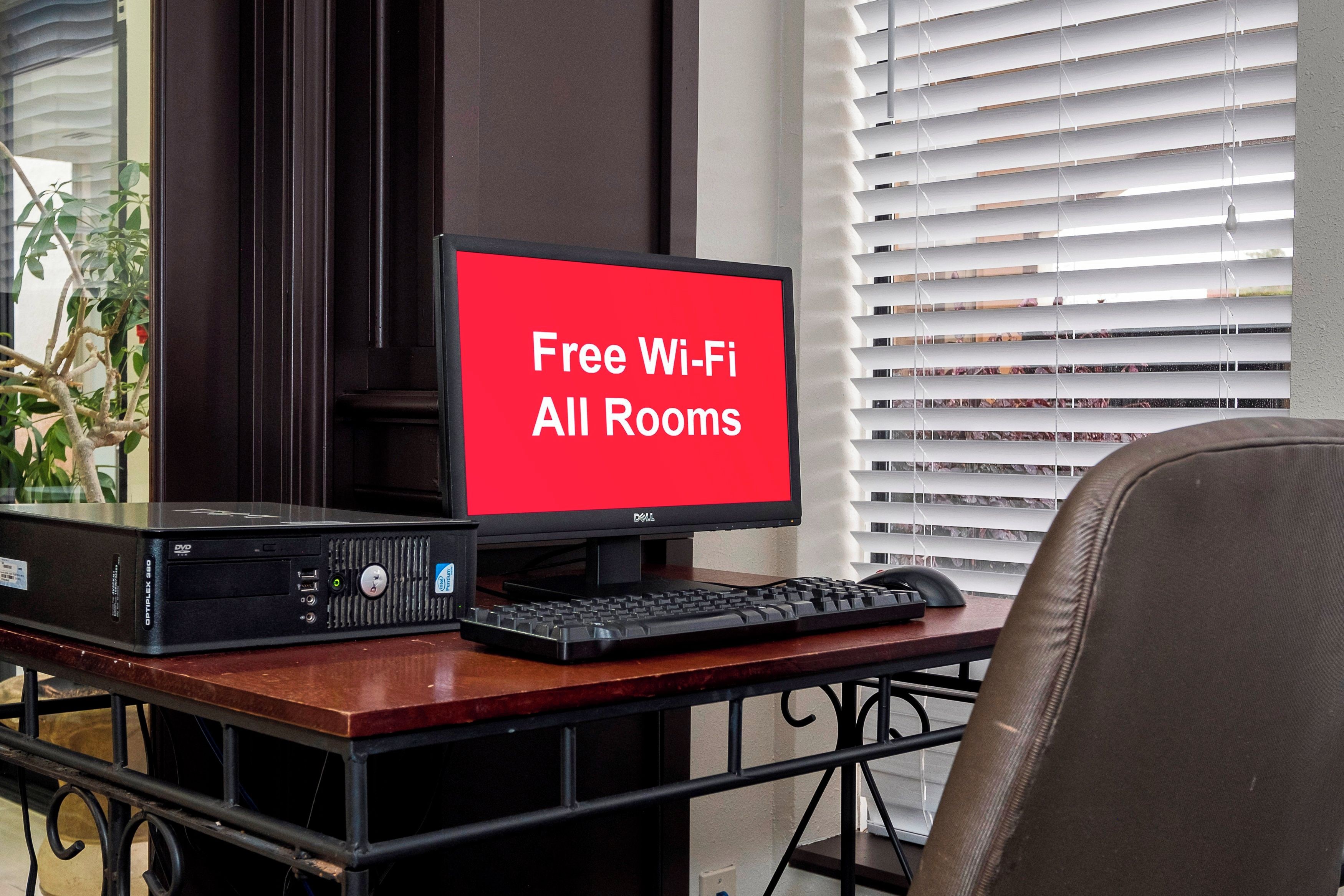 A computer setup with a monitor displaying 'Free Wi-Fi All Rooms' on a hotel desk.