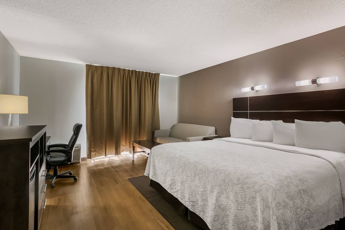 Ein Hotelzimmer mit einem großen Bett, einem Schreibtisch mit Stuhl, einer Couch und einem Fenster mit Vorhängen.