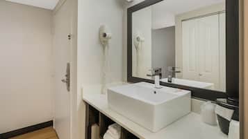 A modern bathroom with a white sink, a large mirror, and two wall-mounted hair dryers.