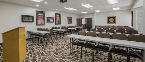 Una sala conferenze con diversi tavoli e sedie, pavimento in moquette e luci a soffitto.
