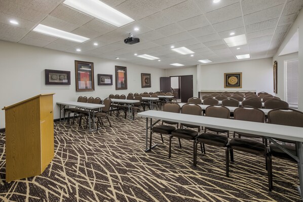 Un salón de conferencias con varias mesas y sillas, piso alfombrado e iluminación en el techo.
