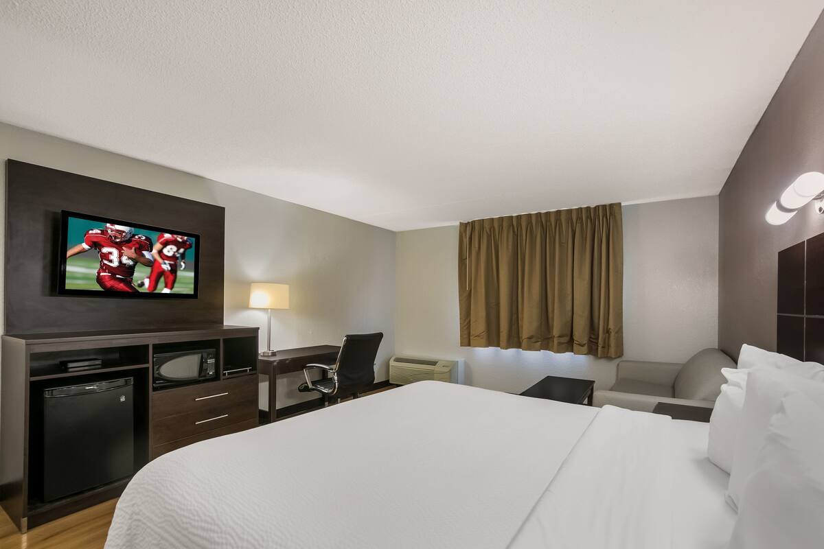 Ein Hotelzimmer mit einem großen Bett, einem Schreibtisch mit Stuhl, einem Fernseher und einem kleinen Kühlschrank.