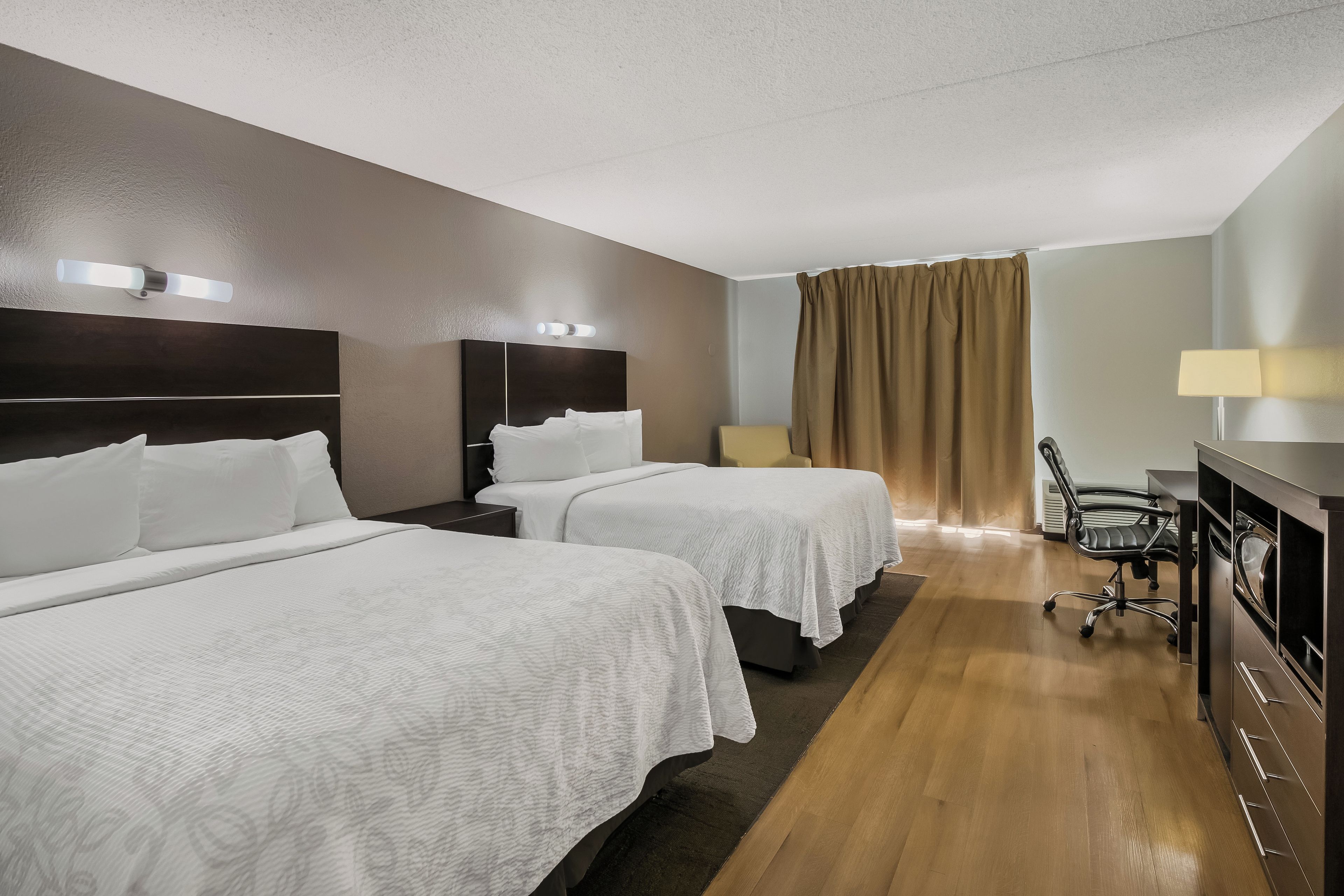 A hotel room with two beds, a desk, a chair, and a window with curtains.
