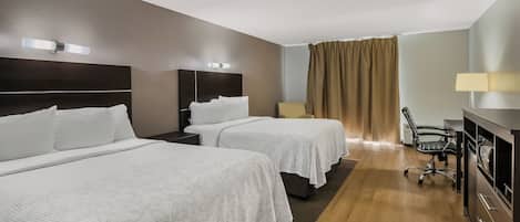 Una habitación de hotel con dos camas, un escritorio, una silla y una ventana con cortinas.