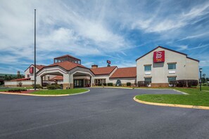 A Red Roof Plus hotel with a central entrance, a parking lot, and a clear sky.