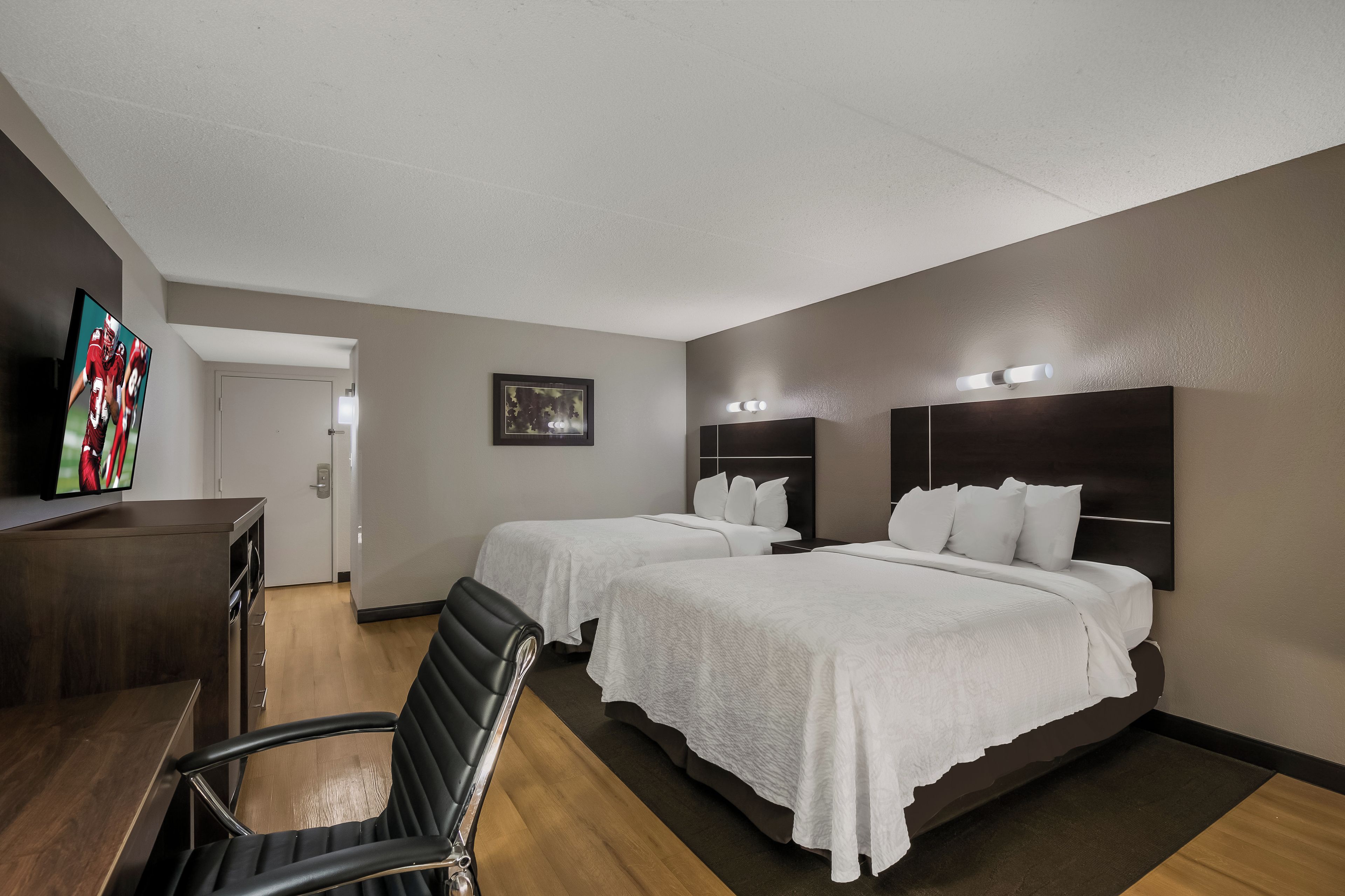 Une chambre d’hôtel avec deux lits, un bureau, une chaise, une télévision et un tableau encadré au mur.