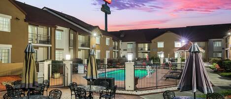 A hotel courtyard with outdoor seating, a swimming pool, and a sunset sky.