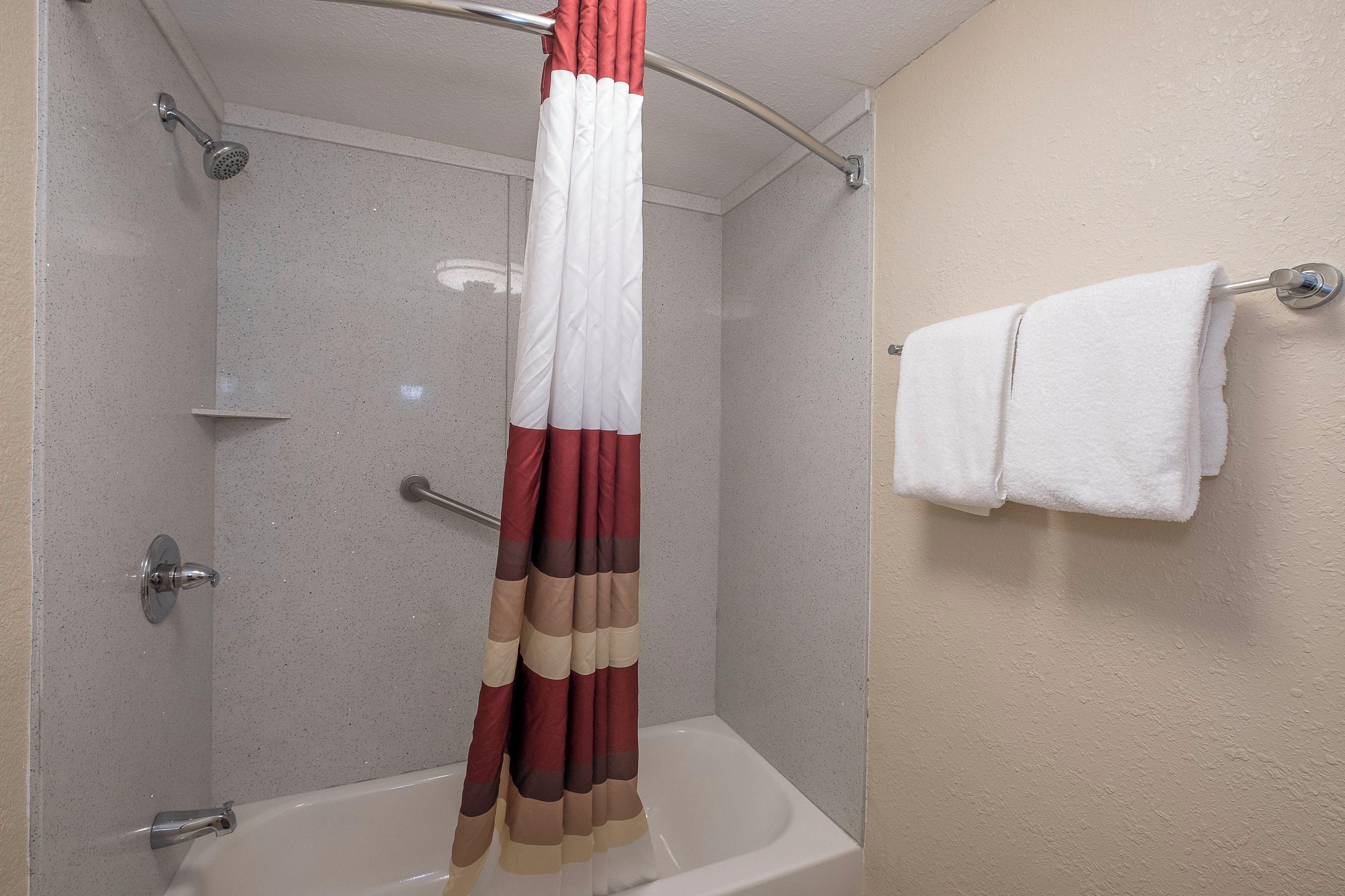 Una ducha con puerta de cristal, una bañera blanca y un perchero con una toalla blanca.