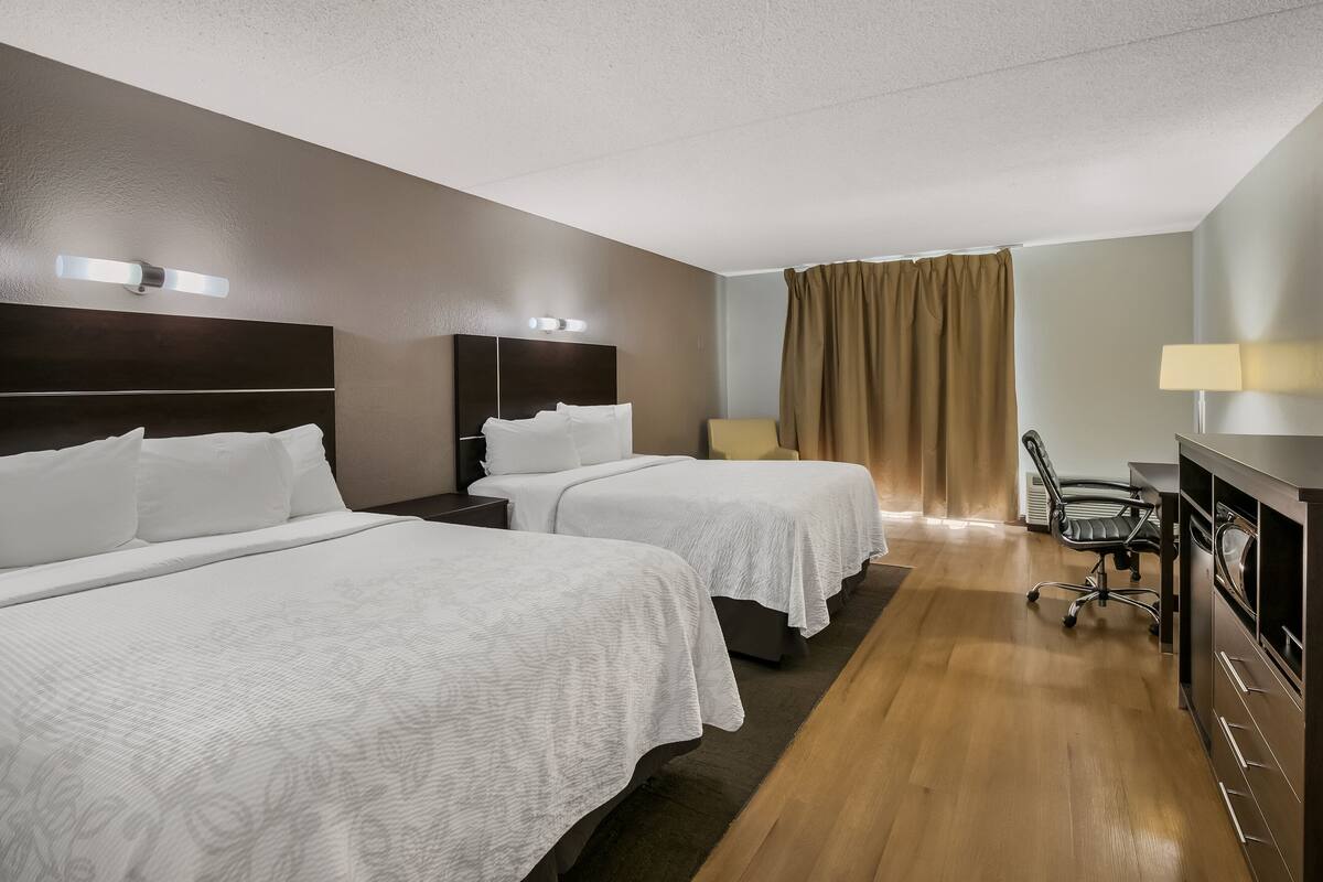 Ein Hotelzimmer mit zwei Betten, einem Schreibtisch, einem Stuhl und einem Fenster mit Vorhängen.